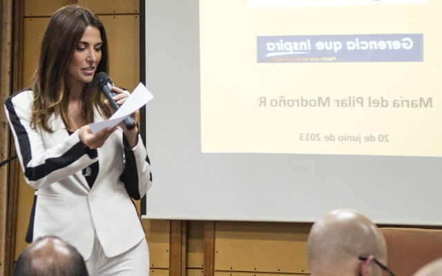 Mujer conferencista elegante con traje blanco y micrófono en una de sus manos evento make it happen a un grupo de personas